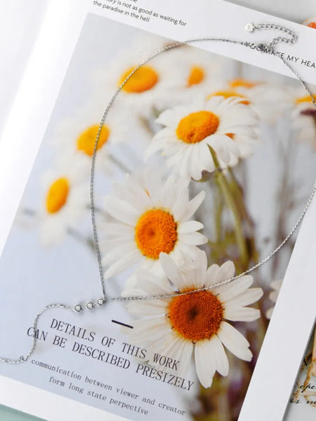 Babe Beachwaer 1.3 carat drop necklace displayed on floral background with white daisies