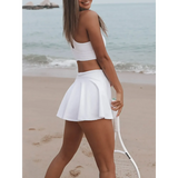Trendsi Criss Cross Cutout Tennis Skort Dress in white worn on beach with tennis racket