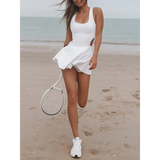 Trendsi Criss Cross Cutout Tennis Skort Dress in white worn on beach holding tennis racket
