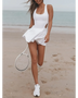 Trendsi Criss Cross Cutout Tennis Skort Dress in white worn on beach holding tennis racket