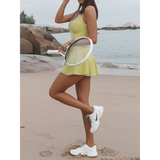 Woman wearing a green Criss Cross Cutout Tennis Skort Dress by Trendsi holding a tennis racket on the beach