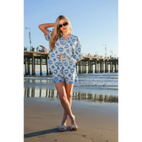 Woman wearing Babe Beachwear tropical blue shorts set with palm print standing on the beach near pier