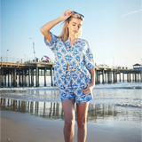 Woman wearing Babe Beachwear tropical blue shorts set with palm tree print on the beach near pier