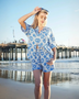 Woman wearing Babe Beachwear tropical blue shorts set with palm tree print on the beach near pier