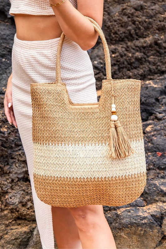 Babe Beachwear two tone straw tote bag with tassel charm held by woman in white outfit