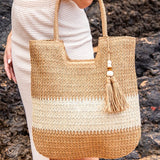 Babe Beachwear two tone straw tote bag with tassel charm held by woman in white outfit