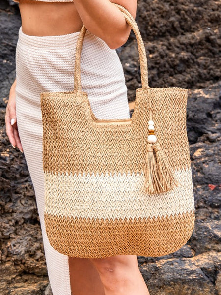 Babe Beachwear two tone straw tote bag with tassel charm held by woman in white outfit