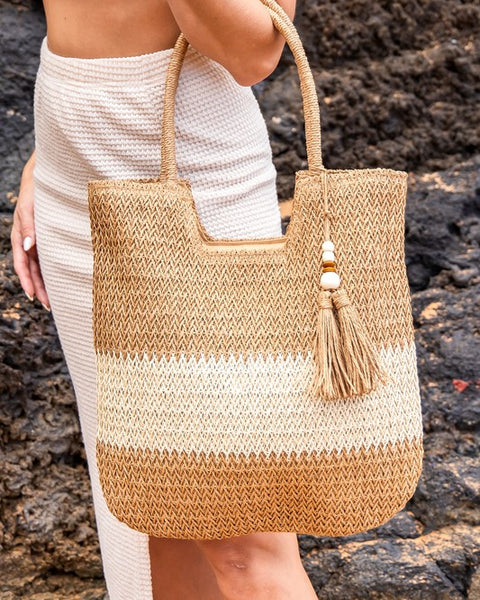 Babe Beachwear two tone straw tote bag with tassel charm held by woman in white outfit