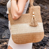 Babe Beachwear two tone straw tote bag with tassel detail carried by woman in white dress