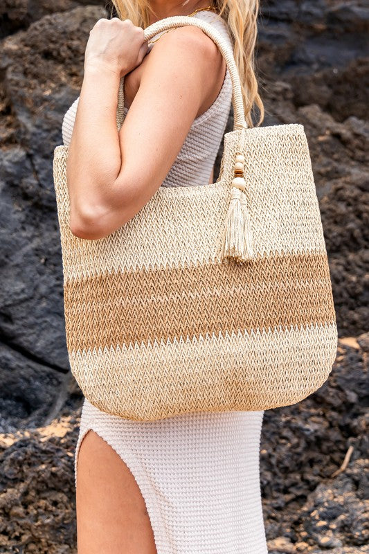 Two tone straw tote bag by Babe Beachwear with beige and natural brown stripes held by woman in white dress
