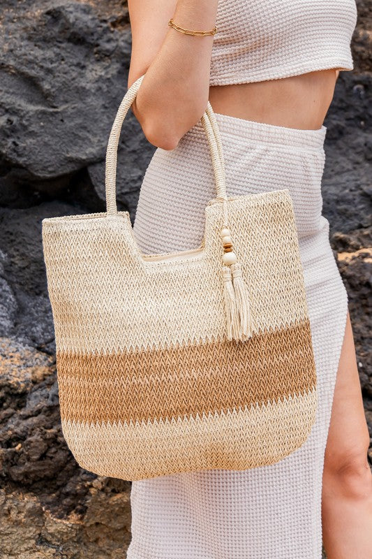 Babe Beachwear two tone straw tote bag with beige and brown stripes carried by woman in white outfit