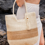 Babe Beachwear two tone straw tote bag with beige and brown stripes carried by woman in white outfit