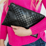 Black studded vacation evening clutch for women held by person in pink sweater and blue jeans