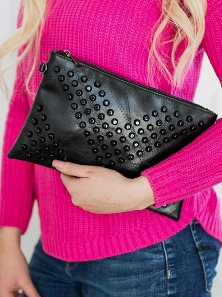 Black studded vacation evening clutch for women held by person in pink sweater and blue jeans