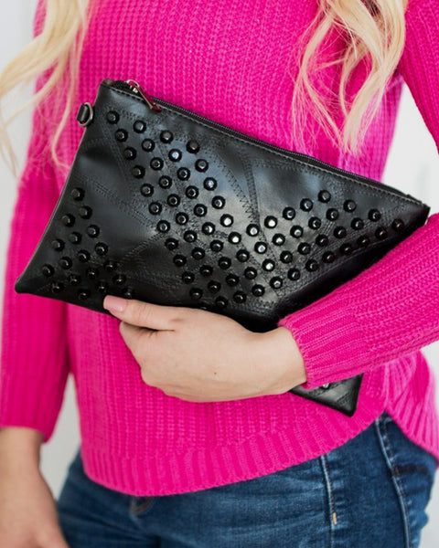 Black studded vacation evening clutch for women held by person in pink sweater and blue jeans