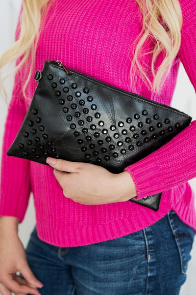 Black studded vacation evening clutch for women held by person in pink sweater and blue jeans