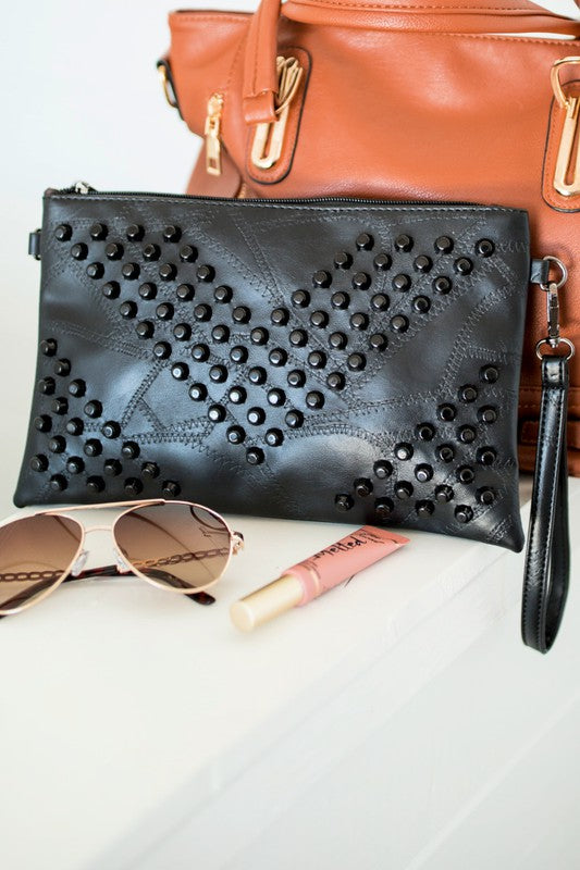 Black vacation evening clutch for women with studded design and wrist strap displayed with sunglasses and lip gloss