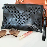 Black vacation evening clutch for women with studded design and wrist strap displayed with sunglasses and lip gloss