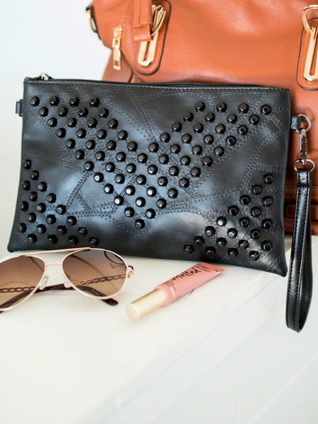 Black vacation evening clutch for women with studded design and wrist strap displayed with sunglasses and lip gloss