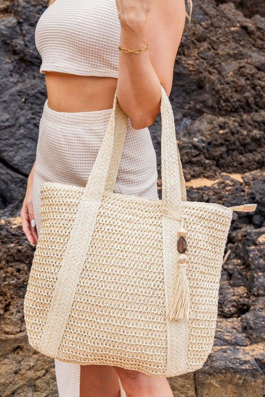 Chic classy woven khaki boho bag with long straps worn by woman in a cream outfit near rocks