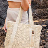 Chic classy woven khaki boho bag with long straps worn by woman in a cream outfit near rocks