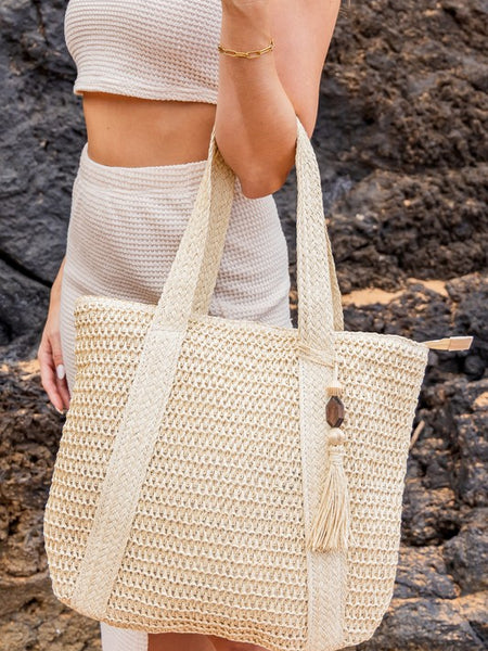 Chic classy woven khaki boho bag with long straps worn by woman in a cream outfit near rocks