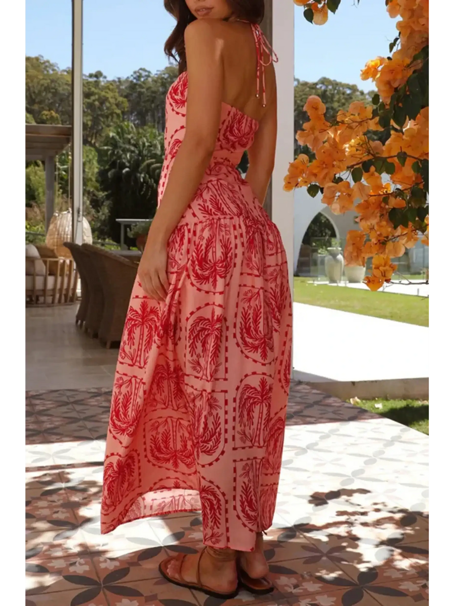 Woman wearing empire waist maxi dress in pink with red patterns featuring a backless design and halter neck