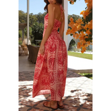 Woman wearing empire waist maxi dress in pink with red patterns featuring a backless design and halter neck