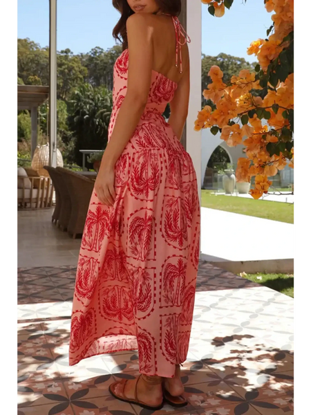 Woman wearing empire waist maxi dress in pink with red patterns featuring a backless design and halter neck