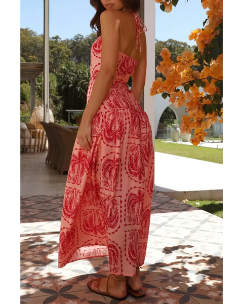 Woman wearing empire waist maxi dress in pink with red patterns featuring a backless design and halter neck