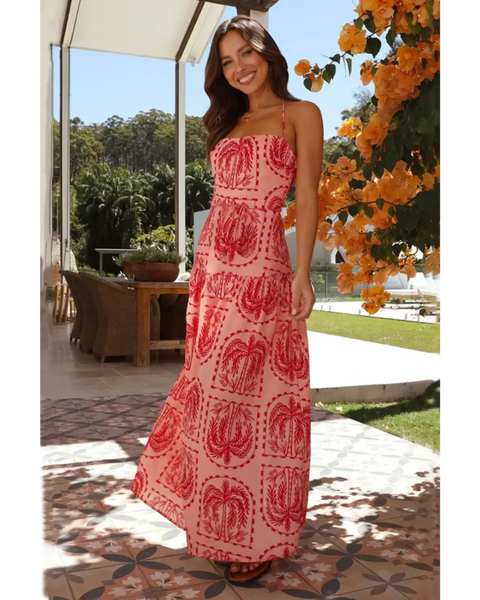 Coral empire waist maxi dress with red and pink tropical print worn by a smiling woman outdoors