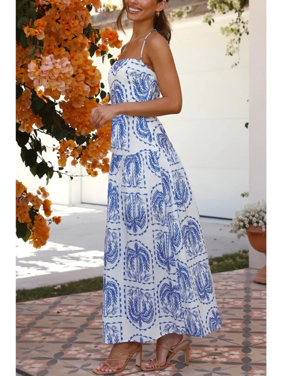 Woman showing side view  blue and white patterned empire waist maxi dress with spaghetti straps worn outdoors