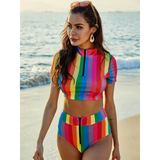 Woman wearing Beach Babes high waisted rainbow swimsuit with short sleeve zip-up top on the beach