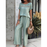 Light green satin pants set with short sleeve top and wide-leg pants accessorized with bracelets and a woven handbag