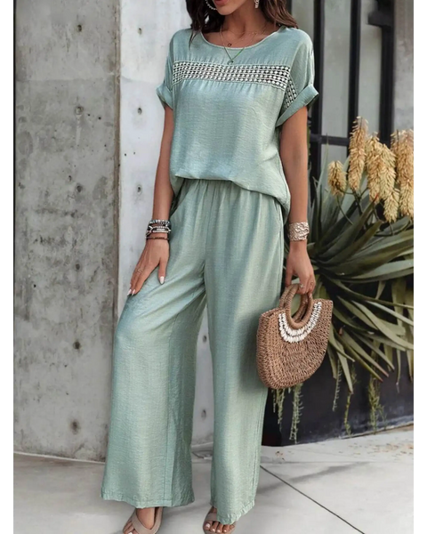 Light green satin pants set with short sleeve top and wide-leg pants accessorized with bracelets and a woven handbag