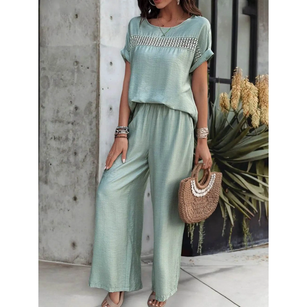 Light green satin pants set with short sleeve top and wide-leg pants accessorized with bracelets and a woven handbag
