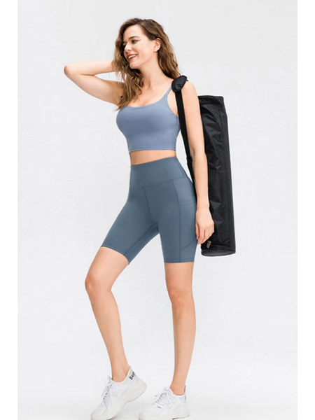 Woman wearing Babe Beachwear women's sports shorts with pockets in blue while carrying a yoga mat