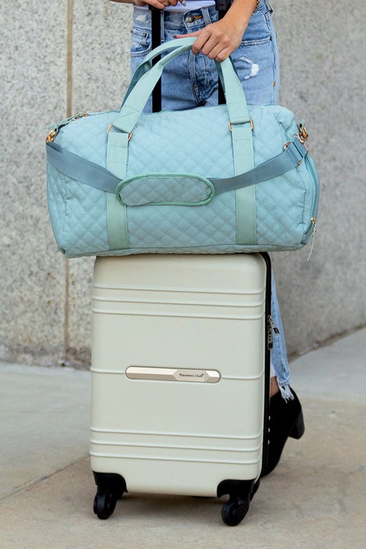 Babe Beachwear Zahra carry on overnight bag in light blue quilted fabric held on top of white rolling suitcase