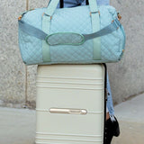 Babe Beachwear Zahra carry on overnight bag in light blue quilted fabric held on top of white rolling suitcase
