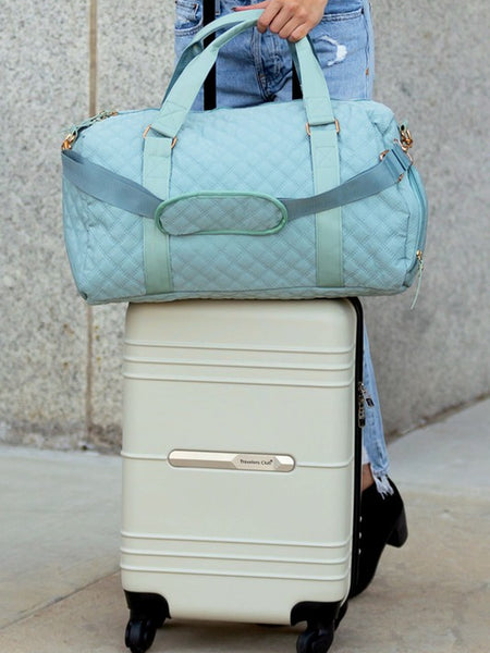 Babe Beachwear Zahra carry on overnight bag in light blue quilted fabric held on top of white rolling suitcase