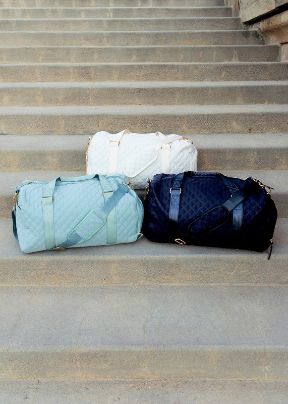Three Babe Beachwear Zahra carry on overnight bags in white, light blue, and navy blue on concrete stairs