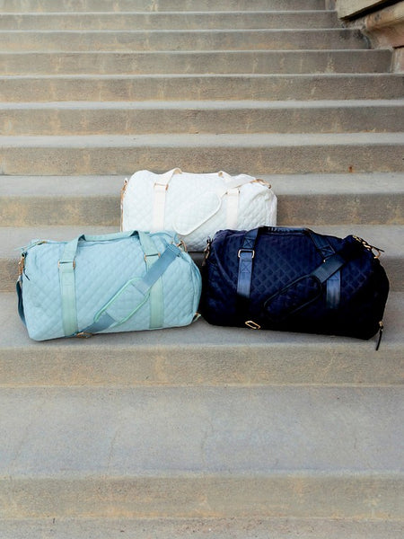 Three Babe Beachwear Zahra carry on overnight bags in white, light blue, and navy blue on concrete stairs